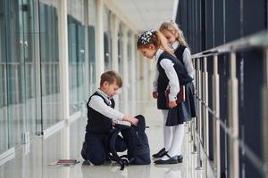 Junge, der auf dem Boden sitzt. Schulkinder in Uniform zusammen im Korridor foto