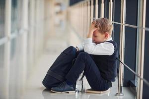 Junge in Uniform sitzt allein und fühlt sich in der Schule traurig. Begriff der Belästigung foto