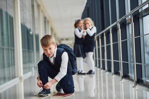 Junge, der auf dem Boden sitzt. Schulkinder in Uniform zusammen im Korridor foto