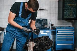 professioneller mechaniker in schwarzer schutzmaske arbeitet mit kaputtem automotor foto