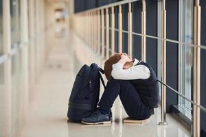 Junge in Uniform sitzt allein und fühlt sich in der Schule traurig. Begriff der Belästigung foto