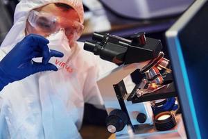 wissenschaftler in weißer schutzkleidung drinnen im labor mit linse mit virustitel darauf foto