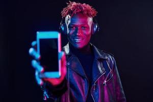 mit Handy und Kopfhörer. futuristische neonbeleuchtung. junger Afroamerikaner im Studio foto