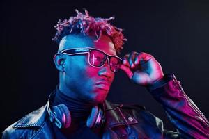 stylische Brille und kabellose Kopfhörer. futuristische neonbeleuchtung. junger Afroamerikaner im Studio foto