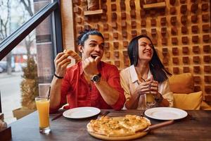 multiethnisches junges paar sitzt drinnen zusammen und isst pizza foto