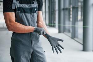 Mann in grauer Uniform, der Handschuhe trägt und sich tagsüber in einem modernen großen Büro auf die Arbeit im Haus vorbereitet foto