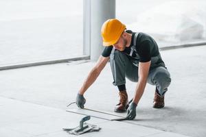 Einbau von Platten. mann in grauer uniform und orangefarbenem schutzhelm arbeitet tagsüber drinnen in einem modernen großen büro foto