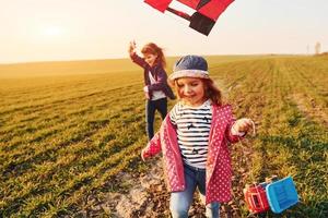 zwei kleine freundinnen haben spaß zusammen mit drachen und spielzeugauto auf dem feld bei sonnigem tag foto