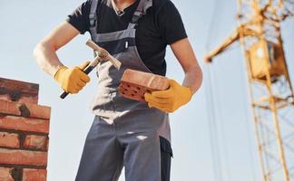 Ziegel halten und Hammer verwenden. bauarbeiter in uniform und sicherheitsausrüstung haben arbeit am bau foto