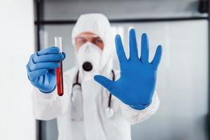 männlicher arztwissenschaftler in laborkittel, defensiver brille und maske hält reagenzglas mit blut foto
