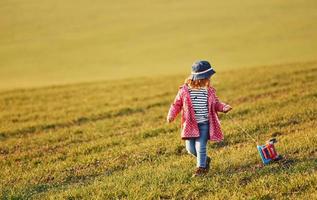 süßes kleines mädchen geht tagsüber mit spielzeugauto auf dem schönen feld spazieren foto