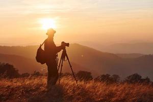 männlicher fotograf, der in der majestätischen landschaft von herbstbäumen und bergen am horizont steht und arbeitet foto