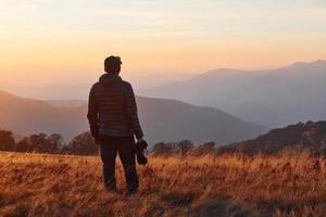 männlicher fotograf, der in der majestätischen landschaft von herbstbäumen und bergen am horizont steht und arbeitet foto