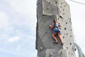 kleines Mädchen in lässiger blauer Kleidung trainiert Klettern im Freien foto
