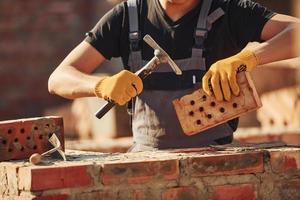 Ziegel halten und Hammer verwenden. bauarbeiter in uniform und sicherheitsausrüstung haben arbeit am bau foto