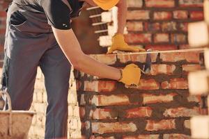 beschäftigt mit Backsteinmauer. bauarbeiter in uniform und sicherheitsausrüstung haben arbeit am bau foto