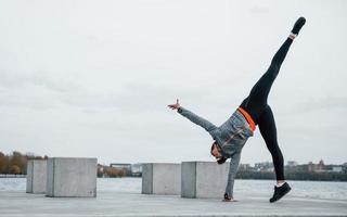 Junges sportliches Mädchen, das tagsüber Parkour-Stunts im Freien in der Nähe des Sees macht foto