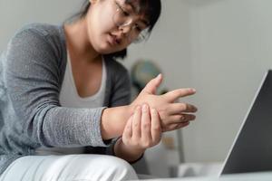 frau, die ihre handschmerzen hält, wenn sie den computer lange benutzt. Office-Syndrom-Konzept. foto