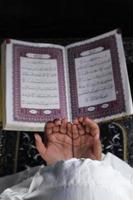 Kinderhand, die mit erhobenen Händen vor dem Koranhintergrund betet. islamisches Konzept foto