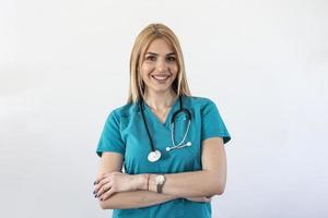 Schöne junge Ärztin schaut in die Kamera und lächelt lächelnd von einer Ärztin, die selbstbewusst mit verschränkten Armen steht foto