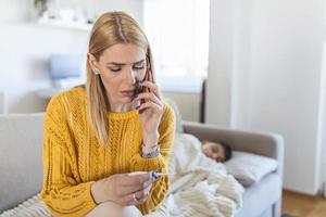 Kranker Junge mit Thermometer im Bett und Mutterhand, die Temperatur misst. mutter überprüft die temperatur ihres kranken sohnes und ruft einen arzt. krankes Kind mit Fieber und Krankheit im Bett. foto