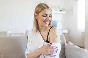Porträt einer Frau, die lächelt, nachdem sie einen Impfstoff erhalten hat. Frau, die ihren Hemdärmel nach unten hält und ihren Arm mit Verband zeigt, nachdem sie die Impfung erhalten hat.