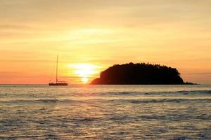 die malerische Aussicht auf ein Meer mit einem kleinen Boot und einer Insel während eines Sonnenuntergangs. Phuket, Thailand. foto