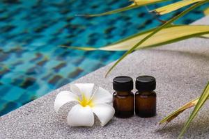 Flaschen ätherisches Aromaöl und Frangipani-Blume auf dem Swimmingpool-Hintergrund für das Spa-Thema. foto