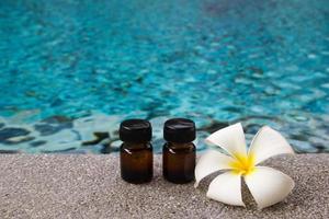 Zwei Flaschen ätherisches Aromaöl und Frangipani-Blume auf dem Swimmingpool-Hintergrund für das Spa-Thema. foto