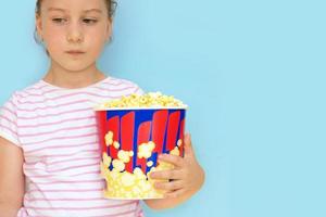 Trauriges Mädchen, das ein großes Glas Popcorn in der Hand auf blauem Hintergrund mit Kopierraum hält foto