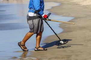 Mann mit einem Metalldetektor an einem Sandstrand foto