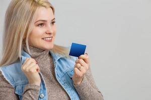 Porträt einer hübschen jungen blonden Frau im Pullover, die eine Kreditkarte zeigt und auf den Kopierbereich einzeln auf blauem Hintergrund blickt foto