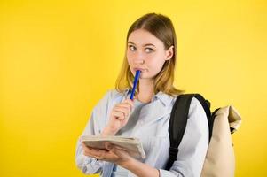 Nahaufnahme einer nachdenklichen kaukasischen Frau, die sich darauf vorbereitet, Notizen in einem Schreibheft auf gelbem Studiohintergrund zu machen. Checkliste der Schule oder Hochschule vorbereiten foto