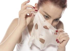Gesichtspflege und Schönheitsbehandlungen. Frau mit einer feuchtigkeitsspendenden Blattmaske auf ihrem Gesicht isoliert auf weißem Hintergrund foto