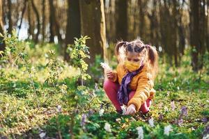 Glückliches kleines Mädchen in Schutzmaske macht tagsüber einen Spaziergang im Frühlingswald foto