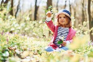 Glückliches kleines Mädchen mit blauem Hut hat tagsüber einen Spaziergang im Frühlingswald foto