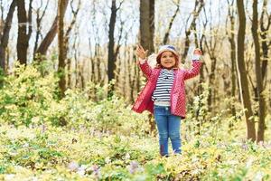 Glückliches kleines Mädchen mit blauem Hut hat tagsüber einen Spaziergang im Frühlingswald foto