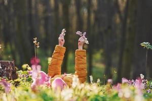 glückliches kleines Mädchen in Freizeitkleidung, das sich tagsüber im Frühlingswald auf den Boden legt foto