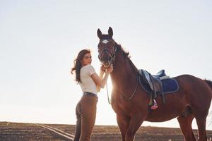 schöner Sonnenschein. junge frau, die tagsüber mit ihrem pferd auf dem landwirtschaftsgebiet steht foto
