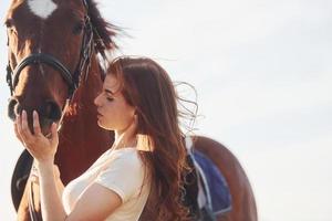 schöner Sonnenschein. junge frau, die tagsüber mit ihrem pferd auf dem landwirtschaftsgebiet steht foto