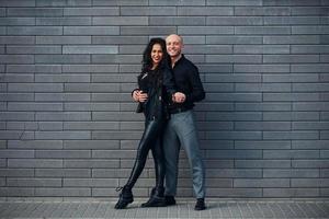 Schönes Paar in schwarzer Kleidung tanzt zusammen gegen die Wand im Freien foto