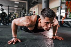 Liegestütze machen. junger sportlicher starker mann in schwarzer kleidung hat trainingstag im fitnessstudio foto