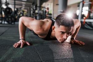 Liegestütze machen. junger sportlicher starker mann in schwarzer kleidung hat trainingstag im fitnessstudio foto