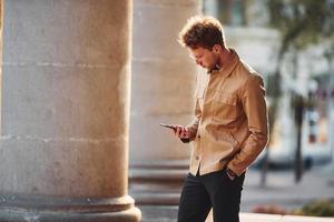 Telefon in der Hand halten. Eleganter junger Mann in formeller, nobler Kleidung im Freien in der Stadt foto