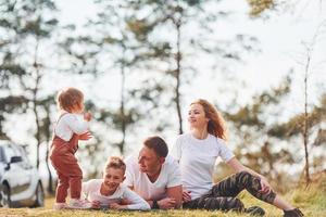 am Boden sitzen und liegen. glückliche familie, die zusammen ein wochenende im freien in der nähe des waldes verbringt. mit Tochter und Sohn foto