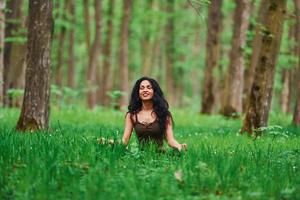 positive brünette in lässiger kleidung, die tagsüber im wald meditiert foto