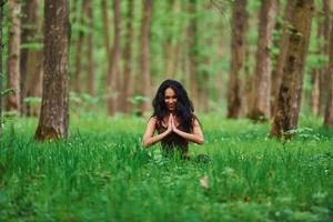 positive brünette in lässiger kleidung, die tagsüber im wald meditiert foto