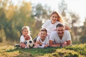 mit Fußball. glückliche Familie, die sich draußen in der Nähe des Waldes hinlegt. mit Tochter und Sohn foto