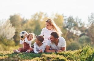 mit Fußball. glückliche Familie, die sich draußen in der Nähe des Waldes hinlegt. mit Tochter und Sohn foto