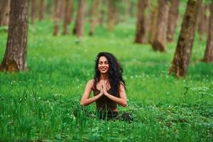 positive brünette in lässiger kleidung, die tagsüber im wald meditiert foto